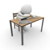 A stressed out figure with head on desk surrounded by books